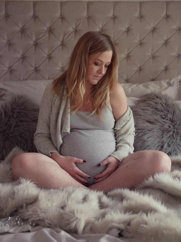 Pregnant woman sat on bed with hands on her baby bump