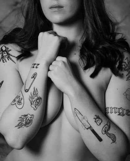Body positive portrait of a brunette with tattoos on forearms with fists clenched