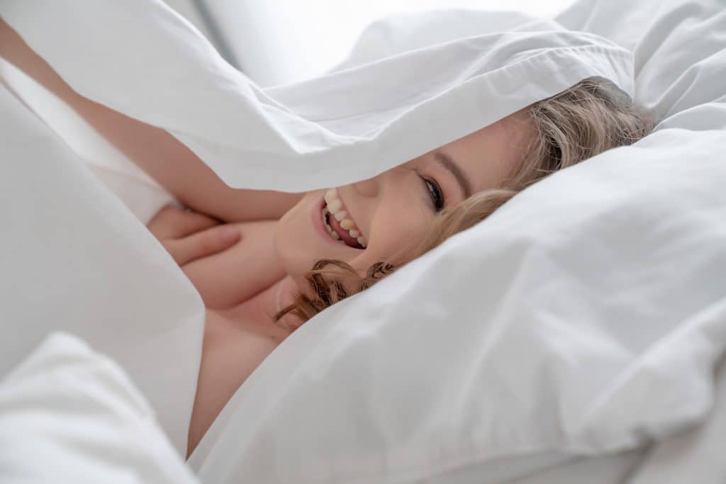 Woman peeping out from underneath white bed sheets